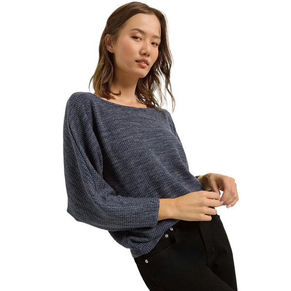 A model showcases a relaxed fit dolman sleeve top in Heather Indigo Haze color, paired with high waisted jeans against a minimalist white background.