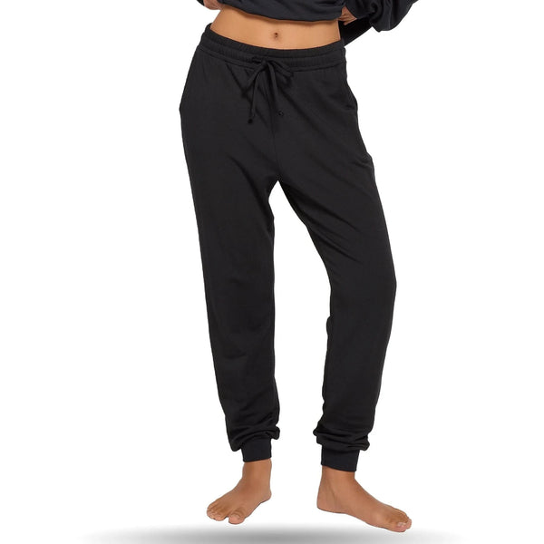 Woman wearing black joggers with elastic waistband and drawstring, standing barefoot against a white background