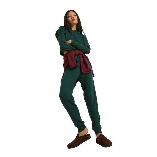 Woman wearing dark green joggers and matching top, burgundy sweatshirt tied at waist, brown slippers