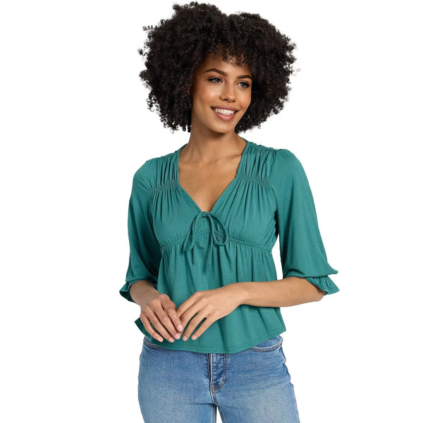 Model showcases a flowy V neck ruffle blouse in soft pastel colors, paired with high waisted jeans against a white background.