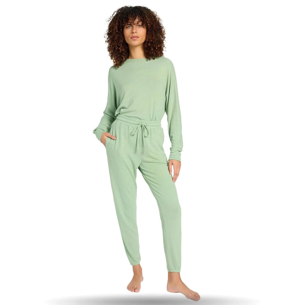 Woman wearing light green joggers and matching top, standing barefoot with one hand in pocket