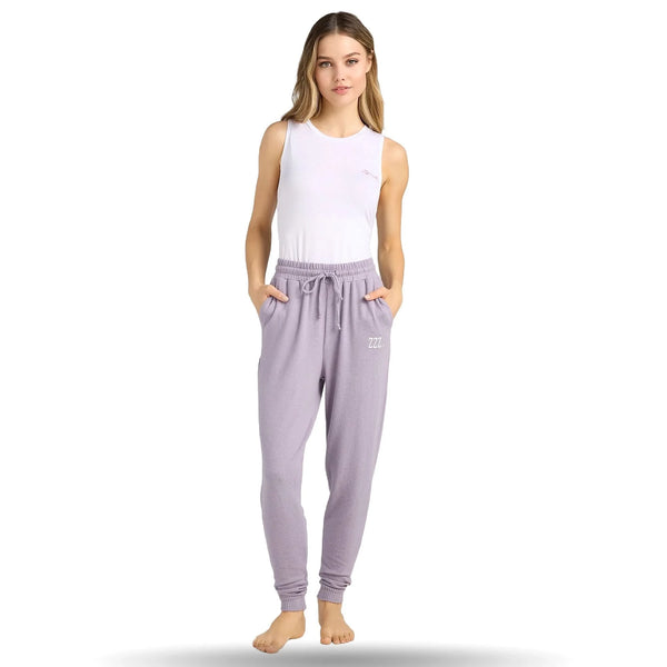 Woman wearing light purple joggers with drawstring waist and white tank top, standing barefoot, hands in pockets