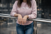 Person wearing a pink sweatshirt with 'LOVE ME NEVER' text, standing against a blurred background.